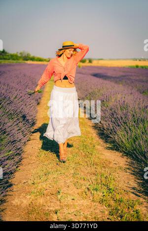 Una donna con un cappello cammina attraverso un campo di lavanda Foto Stock