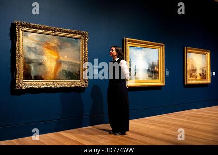 Un assistente di galleria guarda "The Burning of the Houses of Lords and Commons, 16 ottobre" (a sinistra), con "Keelmen Heaving in Coals by Moonlight" (centro) e "Ancient Italy: Ovid Banished from Rome" (a destra) di Joseph Mallord William Turner durante un'anteprima stampa della mostra Turner/Constable alla Tate Britain, Londra. A 250 anni dalla loro nascita, la mostra esplora le vite intrecciate e le eredità di Turner e Constable, con oltre 170 dipinti e opere su carta. Data foto: Lunedì 24 novembre 2025. Foto Stock