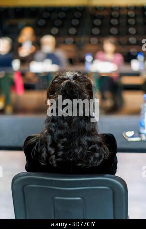Donna con capelli lunghi seduta su una sedia a una conferenza Foto Stock