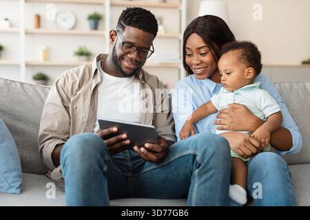 Buona famiglia afroamericana che si diverte con i contenuti educativi su tablet a casa insieme Foto Stock