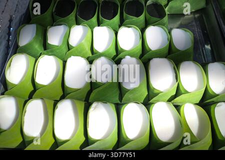 Autentica gelatina tailandese di latte di cocco, in tazze di foglie di banana, con texture cremose a contrasto con avvolgimento verde naturale per un tema dessert sostenibile. Foto Stock