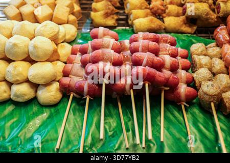 Spuntini di strada tailandesi assortiti su spiedini, tra cui salsiccia con pancetta, polpette di tofu di maiale, involtini di granchio, gnocchi fritti disposti su foglie di banana. Foto Stock