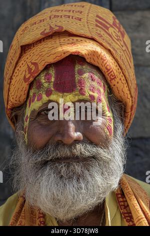 Kathmandu, Nepal - 20 ottobre 2025: Veduta di un uomo sorridente con un volto dipinto che indossa un turbante giallo, con gli occhi che reggono uno sguardo sereno. Foto Stock