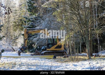 Un escavatore si trova inattivo in un cantiere coperto di neve, circondato dalle condizioni invernali e da un paesaggio tranquillo e ghiacciato Foto Stock