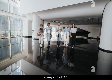 Gruppo di professionisti che camminano attraverso una moderna hall d'ufficio durante una riunione d'affari Foto Stock