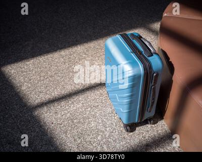 La valigia blu si trova accanto a un sedile marrone sul pavimento macchiato Foto Stock