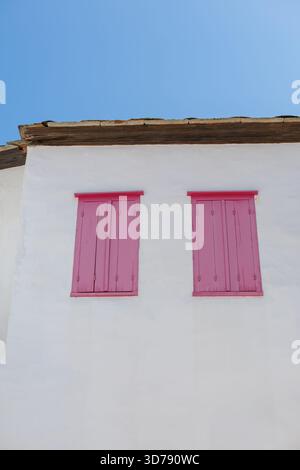 edificio bianco con persiane di legno rosa contro un cielo blu Foto Stock