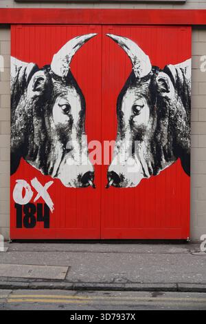 Murale di Street art di due tori di fronte dipinti in bianco e nero su un'audace porta rossa a Edimburgo. Edimburgo, Scozia Foto Stock