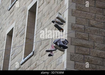 Diverse paia di scarpe appese a cavi sospesi accanto a un edificio in pietra a Edimburgo. Edimburgo, Scozia Foto Stock