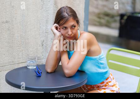 invidiosa giovane donna siede a un tavolo, perduta nel pensiero e annoiata Foto Stock