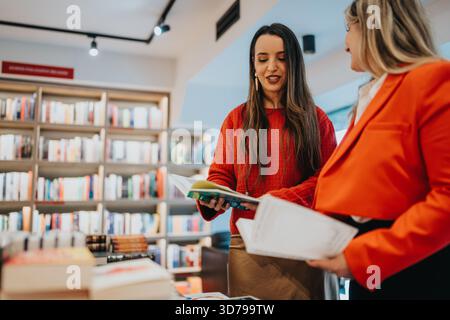 Due donne in una libreria sfogliano gli scaffali e discutono insieme un libro Foto Stock