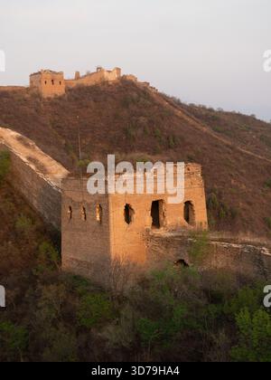 Vista dell'antica grande Muraglia che serpeggia sulle aspre colline, bagnata dal caldo bagliore del sole che tramonta, che testimonia la storia di Pechino e Beiji Foto Stock