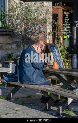 uomo di mezza età seduto da solo al tavolo del pub-giardino guardando il suo smartphone del telefono cellulare. Foto Stock