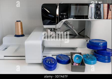 Moderna macchina da cucire e contenitori blu con perni da cucire. Primo piano della postazione di lavoro di una sarta con attrezzature e accessori. Foto Stock