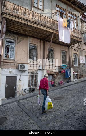 Tbilisi, Georgia. 12 settembre 2025 un vecchio cammina per le stradine acciottolate, passando davanti all'architettura tradizionale del centro storico di Tbilisi, G. Foto Stock