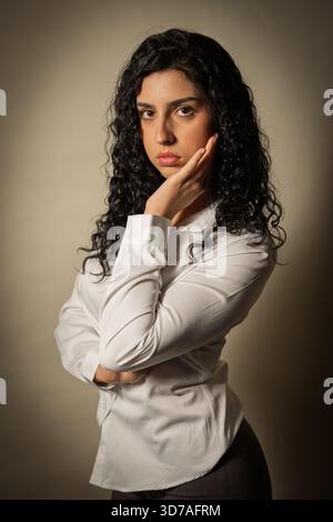 Giovane donna con capelli ricci che pensa seriamente, guardando avanti con un'espressione pensiva Foto Stock