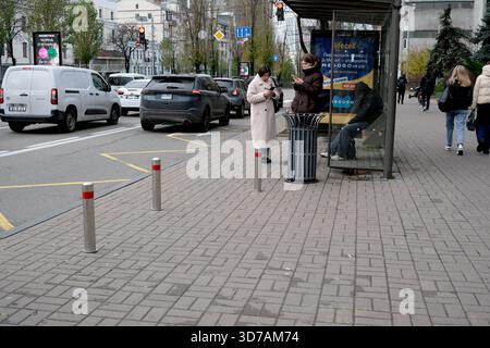 Due donne si trovano alla fermata dell'autobus, mentre altre passano davanti a una vivace strada urbana. 24 novembre 2025, Kiev, Ucraina, Shevchenko Boulevard Foto Stock