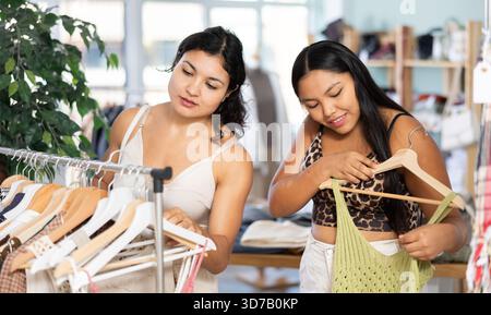 Due giovani donne che scelgono abiti estivi o top in un negozio di abbigliamento Foto Stock