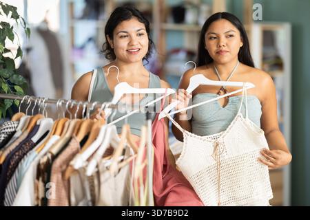 Due giovani donne che scelgono abiti estivi o top in un negozio di abbigliamento Foto Stock
