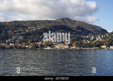 Un paesaggio ad ampio angolo di una costa ripida, rocciosa e densamente boscosa che incontra le calme acque grigie di un grande lago di Como in Italia Foto Stock