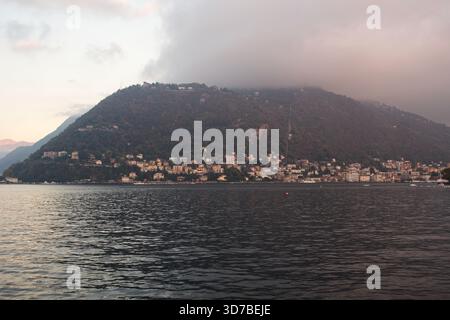 Un paesaggio ad ampio angolo di una costa ripida, rocciosa e densamente boscosa che incontra le calme acque grigie di un grande lago di Como in Italia Foto Stock