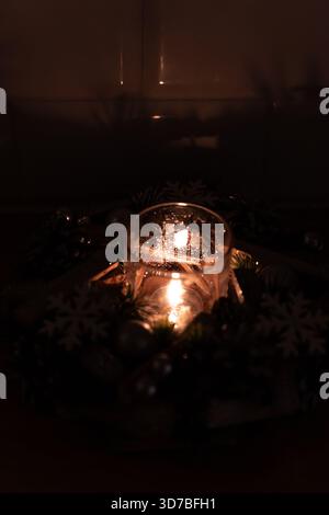 Una vista intima e poco illuminata di una corona dell'Avvento con tre candele a colonna rosse accese su una base verde scuro, che creano un'atmosfera calda e festosa Foto Stock