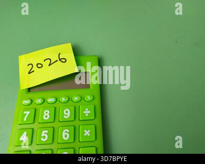 L'immagine mostra una calcolatrice elettronica verde con una nota adesiva gialla sulla parte superiore con il numero 2026. Foto Stock
