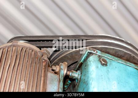 Primo piano di due cinghie tensionate che si attorcigliano tra il motore e le pulegge della macchina con polvere e residui di olio, messa a fuoco selettiva Foto Stock