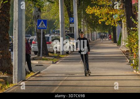 Un giovane guida uno scooter elettrico a Bishkek, nuove tendenze di mobilità nel trasporto urbano moderno. Foto Stock