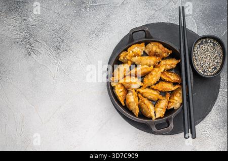 Gnocchi fritti dorati jiaozi cosparsi di sesamo serviti in padella nera su una superficie di pietra brillante, perfetto spuntino asiatico Foto Stock