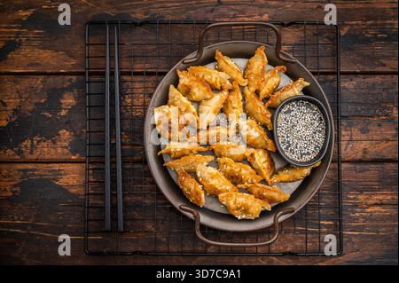 Gnocchi di mandu fritti croccanti con salsa di sesamo su fondo di legno. Adesivi fritti d'oro in una piastra di metallo rustica Foto Stock