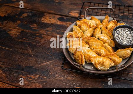 Gnocchi di mandu fritti croccanti con salsa di sesamo su fondo di legno. Adesivi fritti d'oro in una piastra di metallo rustica Foto Stock