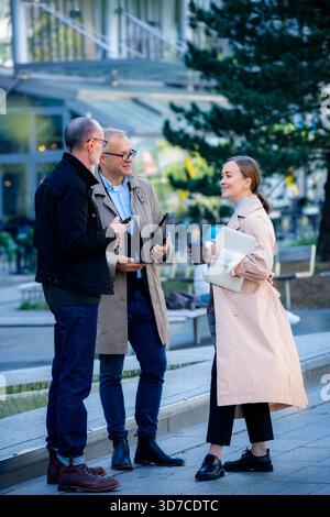 Momento di vita aziendale urbano: Professionisti di mezza età che si incontrano all'aperto, collaborano con laptop e telefoni, sorridono e discutono di lavoro al caffè Foto Stock
