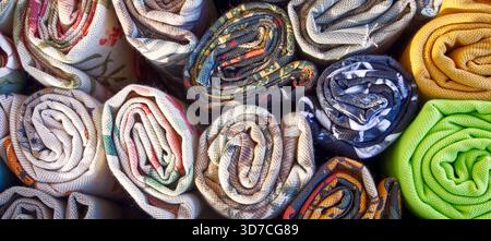 Rotoli di tessuto con diversi motivi e colori. Vista ravvicinata dei tessuti in un mercato, pronti per l'artigianato e il fashion design Foto Stock