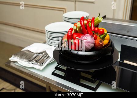 Una vivace disposizione di verdure fresche, tra cui peperoni, pomodori e cipolle, presentate ad arte su un piatto nero. perfetto per migliorare la cena Foto Stock