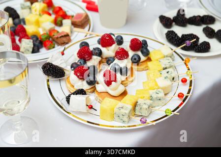Un elegante brunch con formaggio spiedato e frutta, splendidamente esposto. il piatto include bacche colorate, formaggi assortiti e pinea Foto Stock