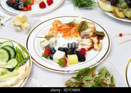 Un piatto ben organizzato che presenta un assortimento di formaggi, frutta fresca e verdi frondosi su una tovaglia bianca. perfetto per riunioni eleganti Foto Stock