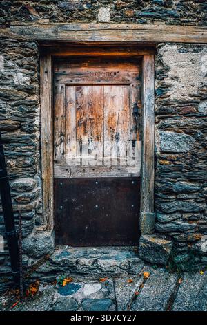 Vecchia porta in legno intemprato con piastra in metallo arrugginito e maniglia nera, inserita in una tradizionale facciata in pietra Foto Stock