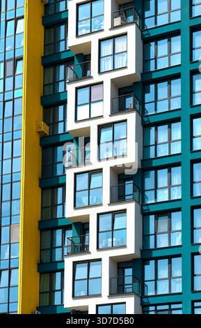 Frammento di un moderno edificio residenziale con facciata colorata. Balconi geometrici bianchi e grandi finestre in vetro blu si distinguono contro un giallo audace Foto Stock