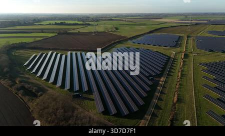 Veduta aerea dei pannelli solari che si crogiolano alla luce soffusa del sole sullo sfondo di campi verdi e strutture lontane, Newmarket, Inghilterra, Regno Unito Foto Stock