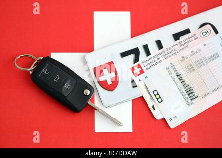 Targa Svizzera e chiave di accensione sulla bandiera svizzera primo piano. Patente di guida e concetto di immatricolazione Foto Stock