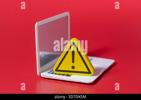 Un cartello di avvertimento giallo con un punto esclamativo posizionato su un notebook. Sicurezza informatica, errore del computer, avviso di sistema, concetto di pericolo online. Foto Stock