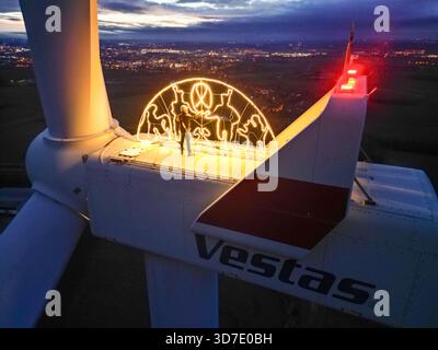Lipsia, Germania. 24 novembre 2025. Steffen Flämig controlla l'illuminazione su un arco di candele sovradimensionato su una turbina eolica. L'arco di sei metri con il motivo Schwarzenberg splende a un'altezza di 140 metri sulla navicella della turbina eolica. Flämig ora vuole premere di nuovo il pulsante per il primo Avvento e accendere il suo arco di candela in alto sopra il Vorerzgebirge di notte. (Vista aerea con drone) credito: Jan Woitas/dpa/Alamy Live News Foto Stock