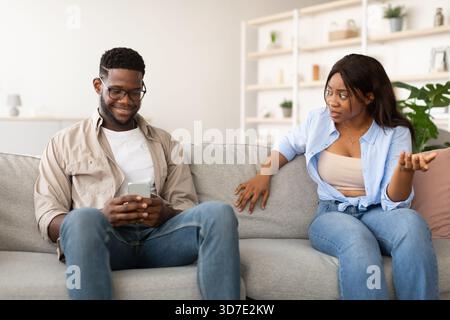Una donna infelice affronta Man on Couch in merito al suo utilizzo del telefono durante una conversazione seria Foto Stock