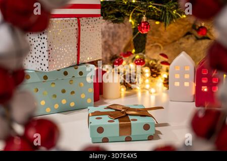 Una disposizione festiva di scatole regalo di Natale confezionate, ciascuna legata a nastri decorativi. Luci gialle calde, pinne e case in miniatura. Foto Stock
