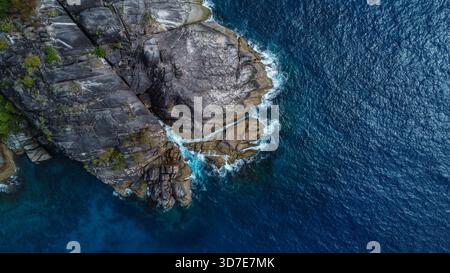 La massiccia scogliera di granito scuro e la Foresta tropicale incontrano il profondo Oceano Foto Stock