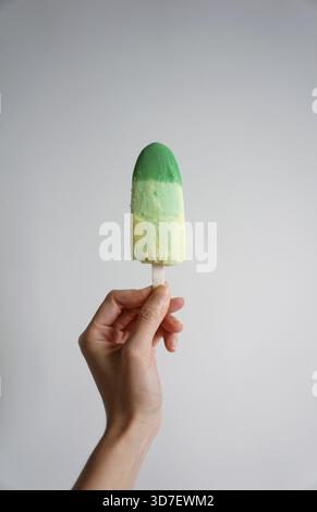 Mano tagliata con una bacchetta di gelato verde su sfondo bianco Foto Stock