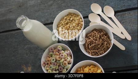 Con cinque ciotole bianche che contengono cereali su un tavolo di legno scuro, bottiglia di latte e cucchiai Foto Stock