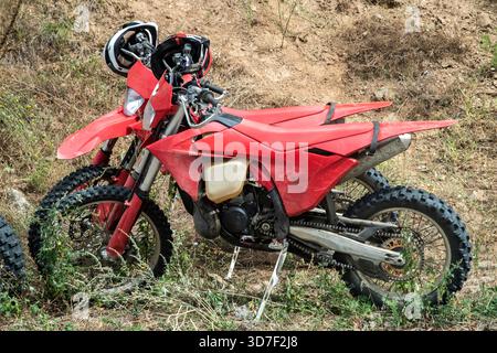 Due motociclette rosse fuoristrada parcheggiate su terreni asciutti con caschi appoggiati sul manubrio in condizioni esterne difficili Foto Stock