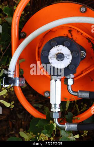 Primo piano di un avvolgitubo industriale arancione con collegamenti idraulici Foto Stock